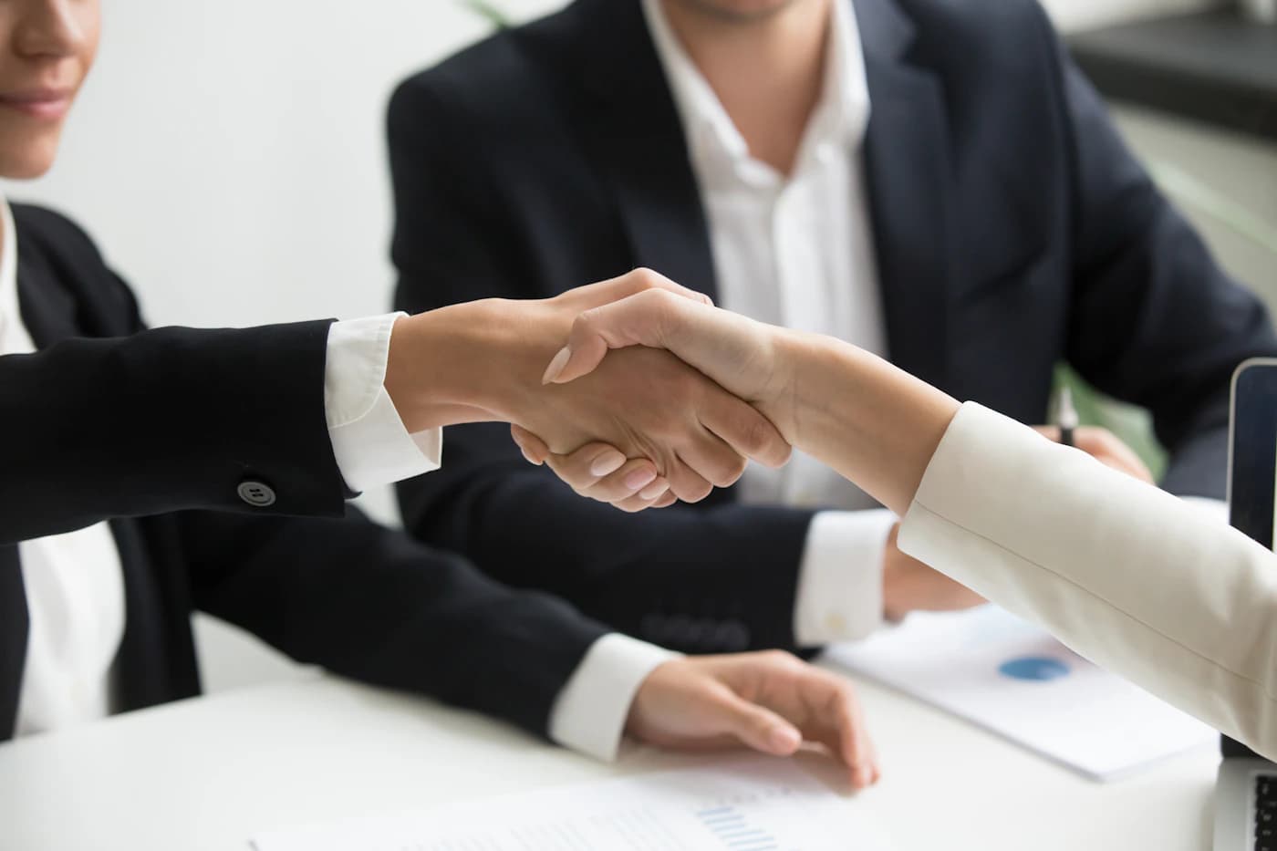 Partners shaking hands over a document at a laptop